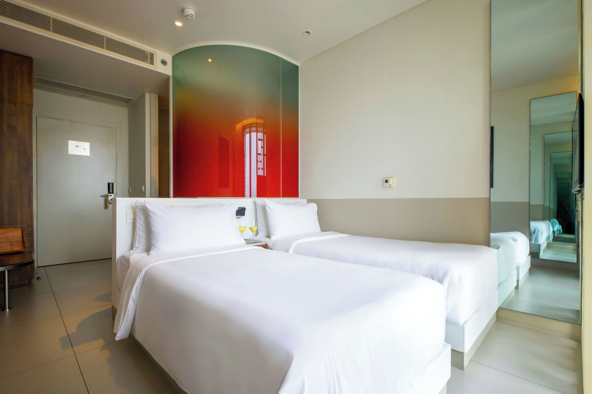 Habitación de hotel con dos camas, un espejo grande y una puerta que da a otra habitación.