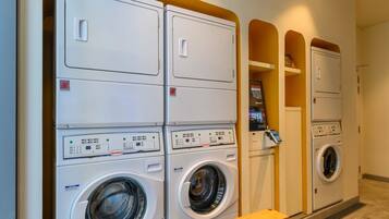 A laundry facility with multiple stacked washing machines and dryers, a control panel, and a small wooden stool.