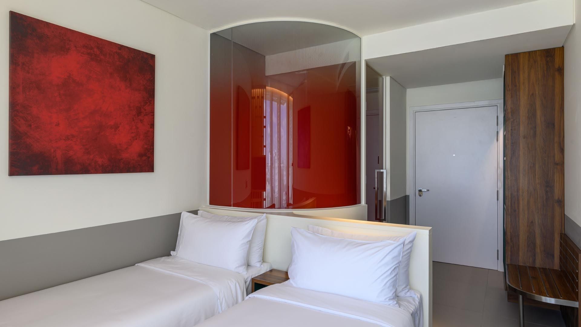 Una habitación de hotel con una cama, una mesita de noche, un espejo, un cuadro abstracto rojo y un armario de madera.