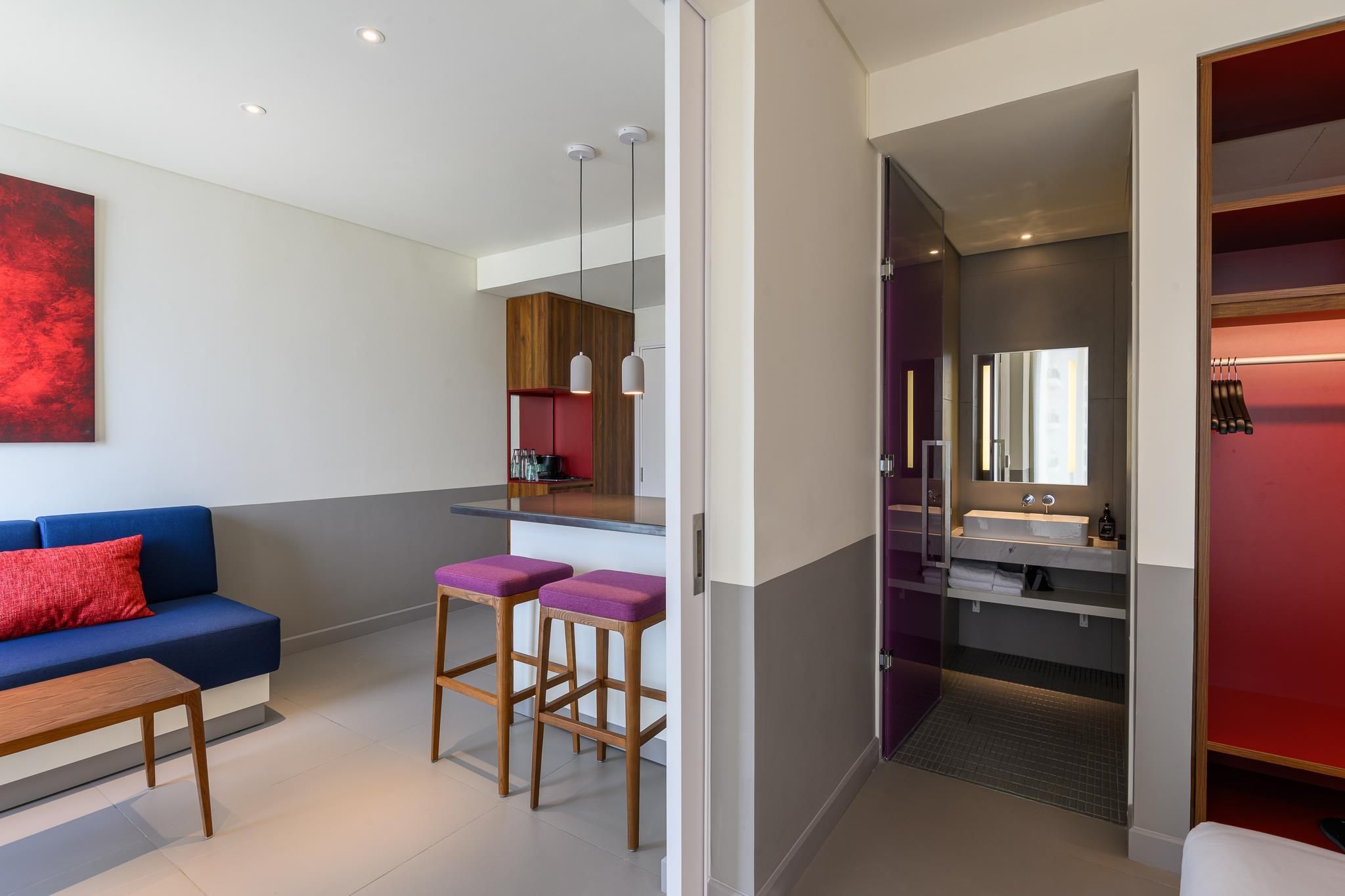 A modern living room with a blue sofa, wooden coffee table, and purple bar stools.