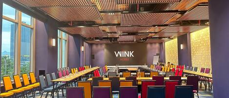 A conference room with a long table, colorful chairs, and a WINK Hotels sign on the wall.