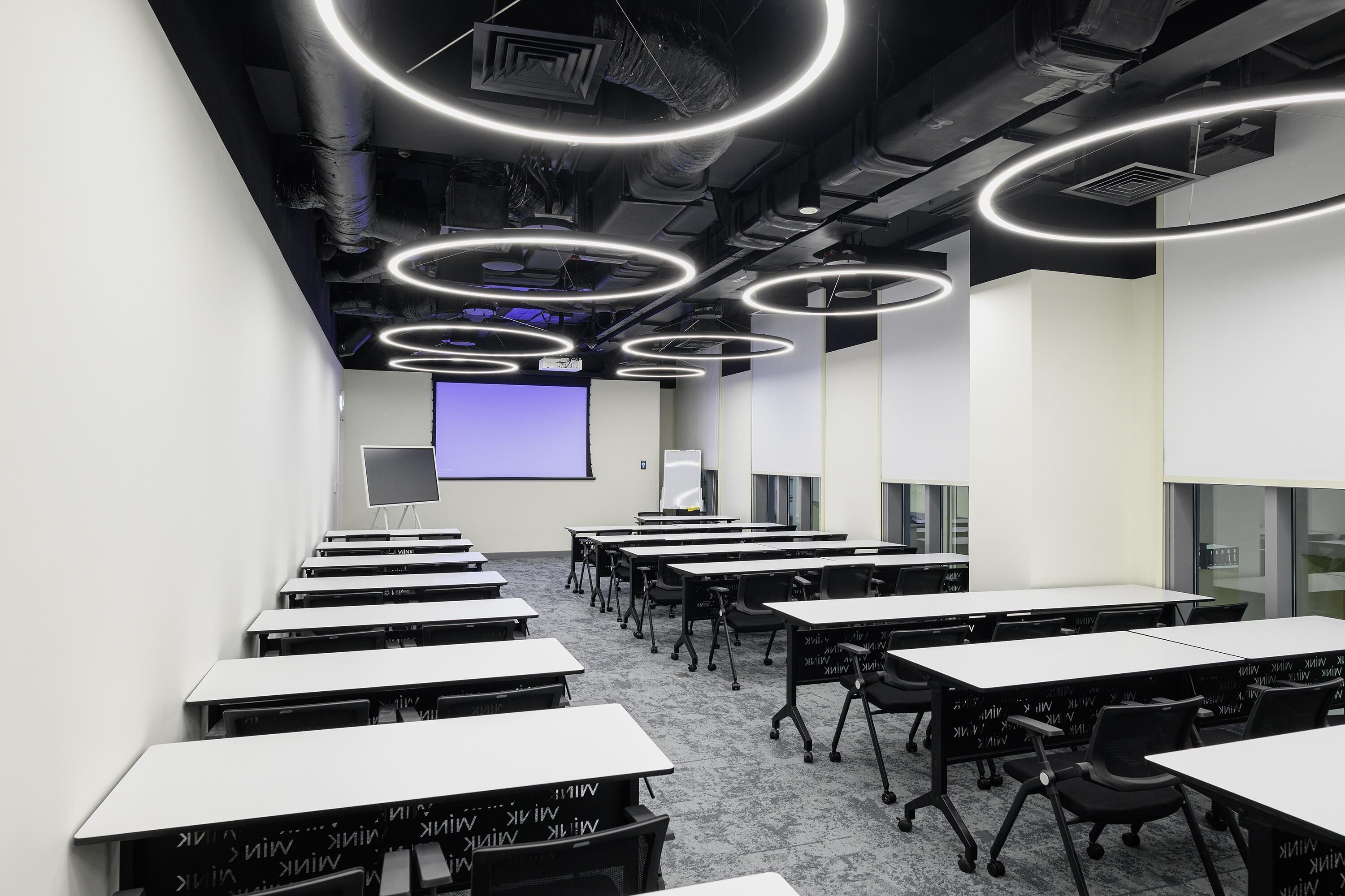 A conference room with multiple tables, chairs, a projector screen, and a whiteboard.