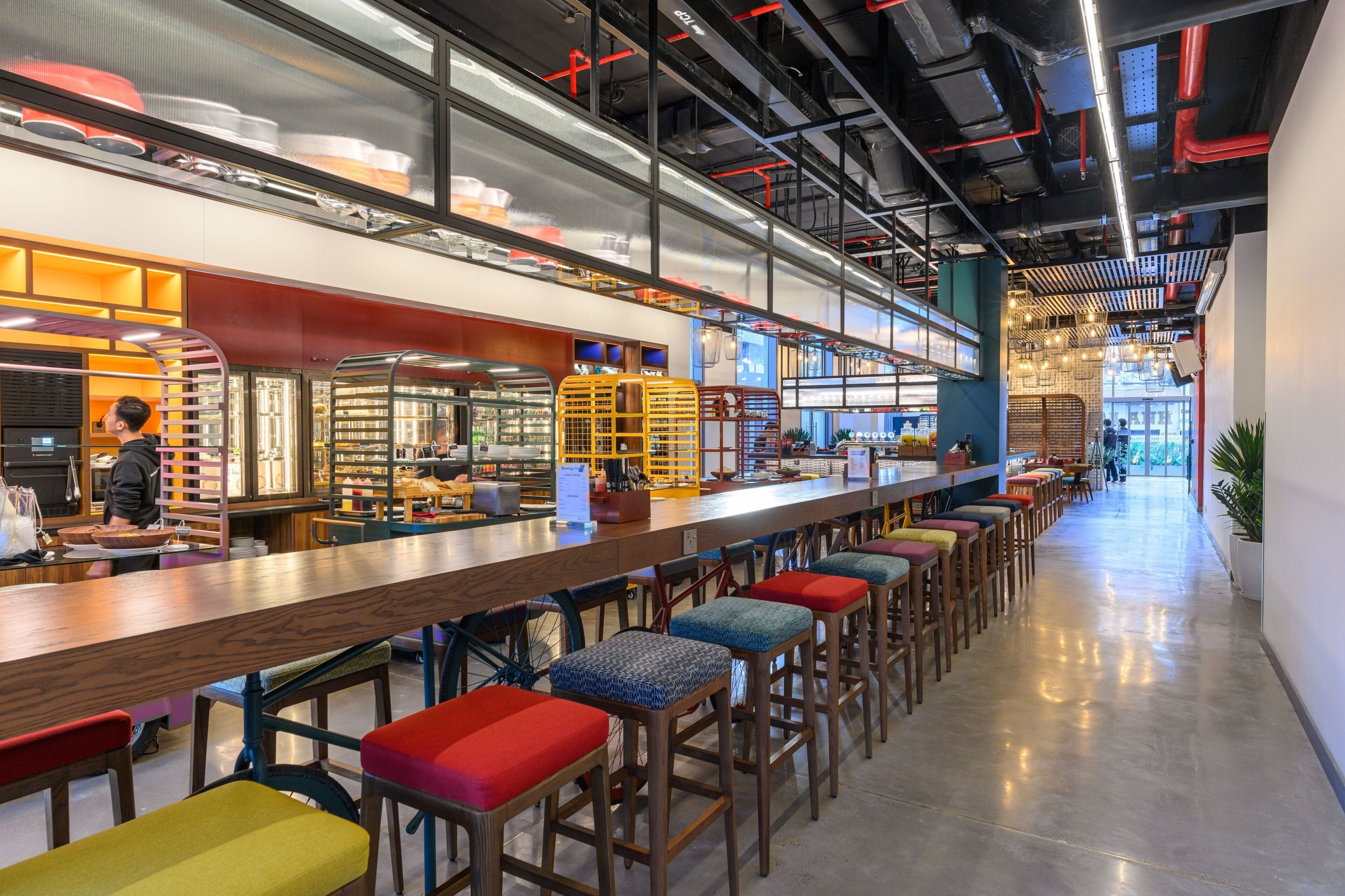 A modern bar area with high stools, a long counter, and a person working behind the bar.