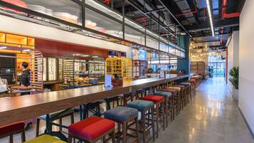 A modern bar area with high stools, a long counter, and a person working behind the bar.