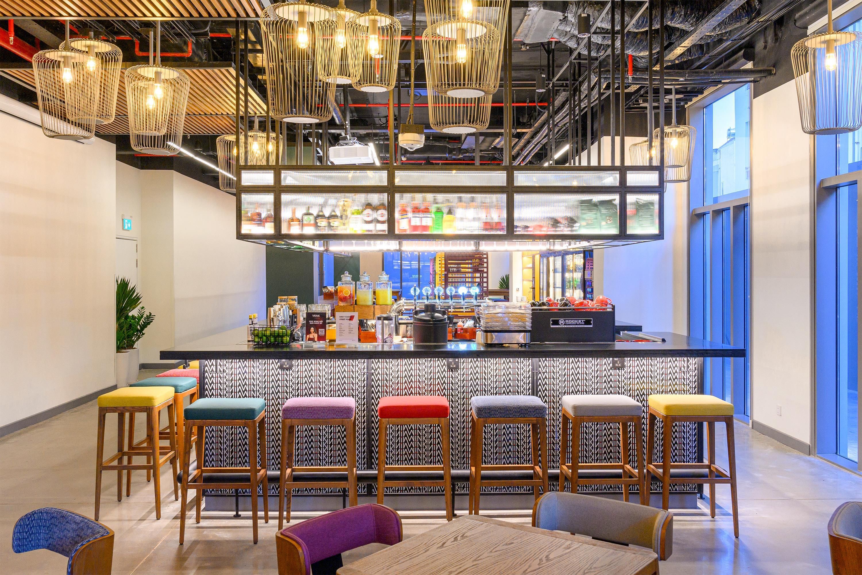 Uma área de bar moderna com banquetas, balcão e luminárias pendentes.