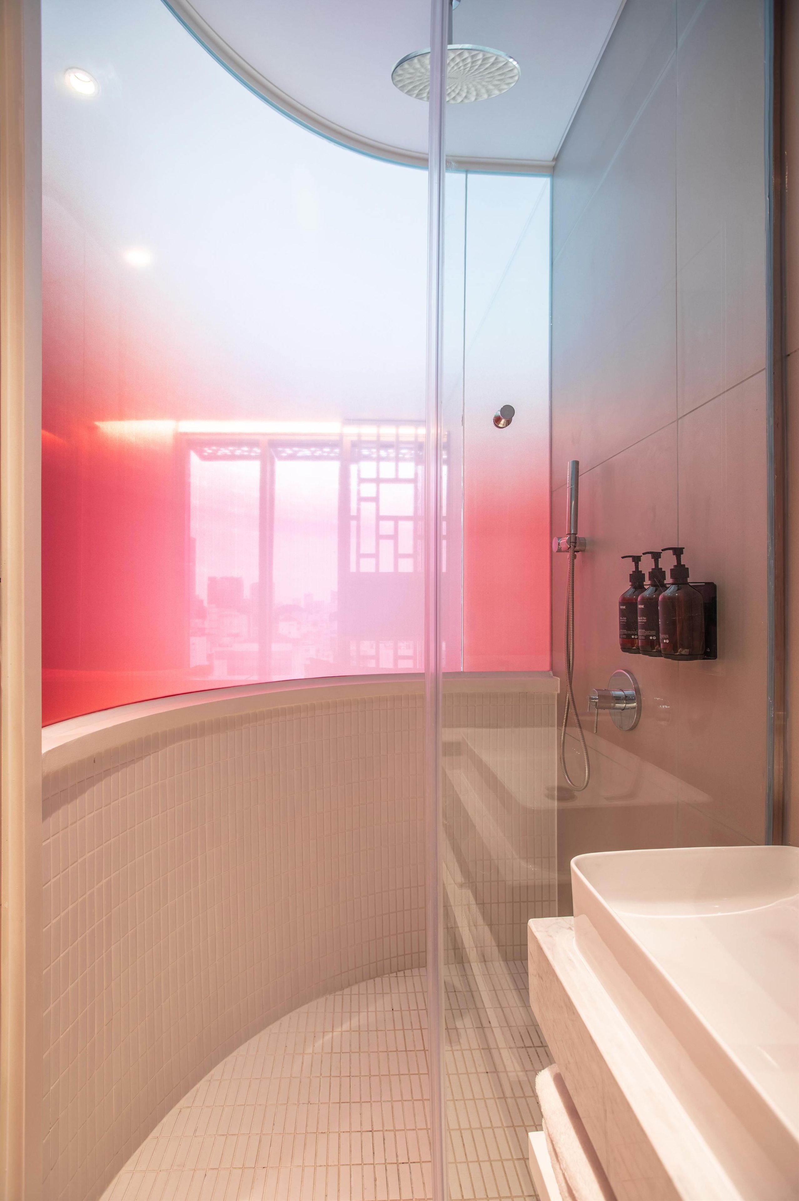 A modern bathroom with a glass shower enclosure, a bathtub, and a wall-mounted soap dispenser.