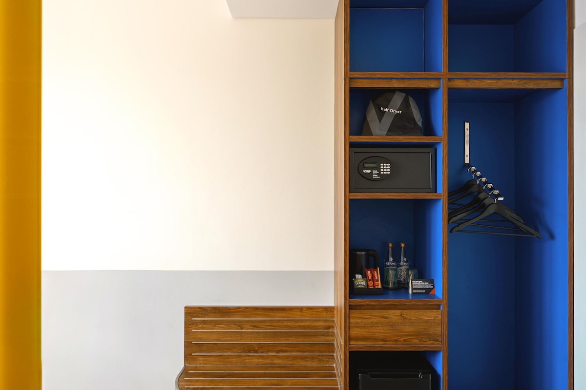 Una habitación moderna con un banco de madera, un mueble azul con estantes, un electrodoméstico negro y un par de pantuflas.
