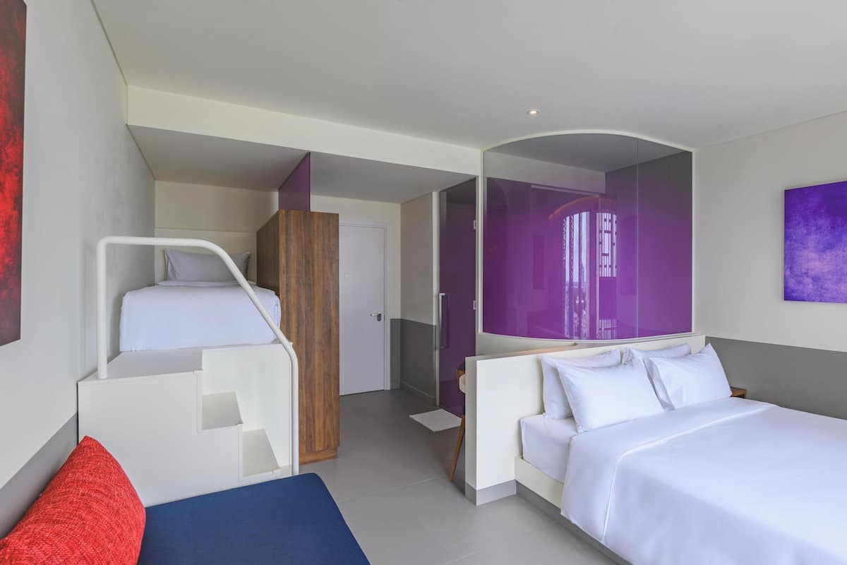 A modern hotel room with a bed, a sofa, a desk, and a bathroom.