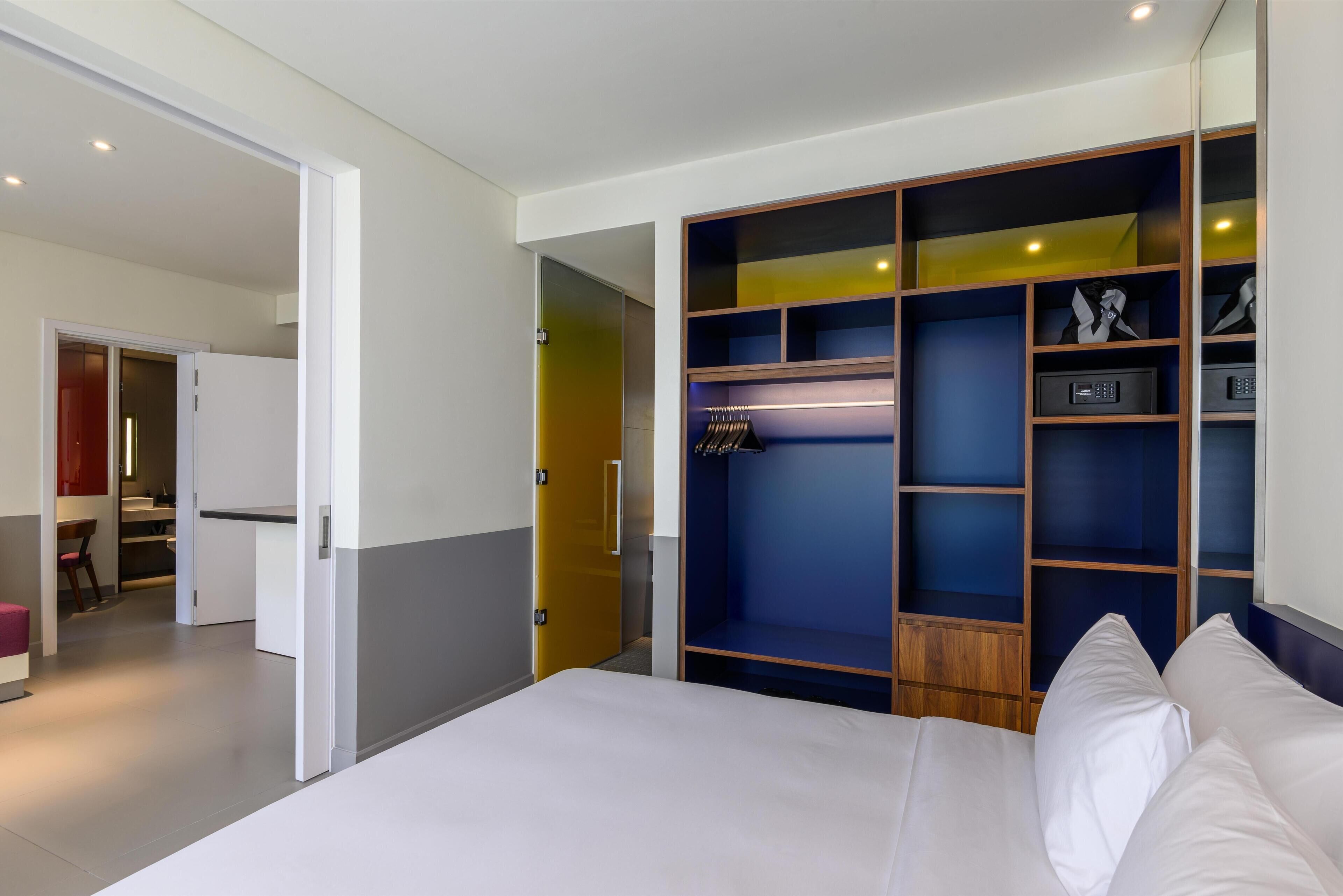 A bedroom with a bed, a wardrobe with shelves, and a desk with a chair.