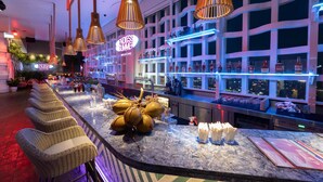 A bar area with wicker chairs, a marble counter, and a city view through the windows. - Wink Cantho Centre, Unscripted by Hyatt - 24 Hours stay (Can Tho)