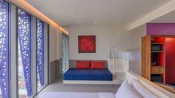 A modern bedroom with a bed, a red pillow, a blue mattress, a red abstract painting, and a bookshelf.