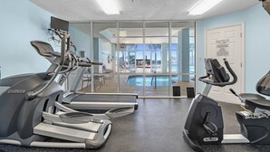 Une salle de sport équipée de tapis de course, d’un appareil elliptique et d’un espace piscine visible à travers des portes vitrées.