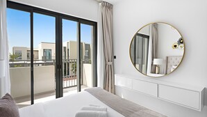Une chambre d’hôtel moderne avec un grand lit, un miroir rond et un balcon offrant une vue sur les immeubles.