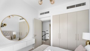 Une chambre à coucher moderne avec un grand miroir rond, un lit avec des serviettes roulées, une commode blanche et un dressing.
