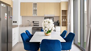Une cuisine moderne avec un coin repas, comprenant une table blanche, des chaises bleues et un vase rempli de fleurs blanches.