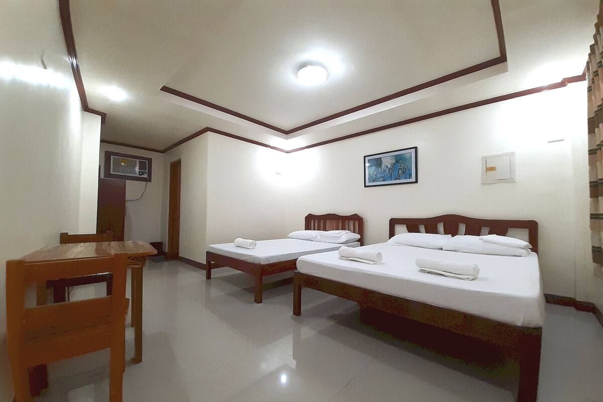 A hotel room with two single beds, a wooden chair, a desk, and a ceiling light.