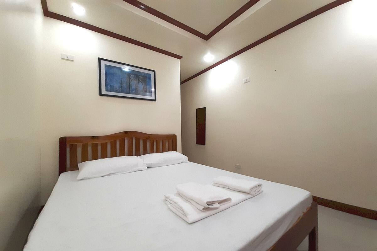 A neatly made bed with white linens and towels, a wooden headboard, and a framed picture on the wall.
