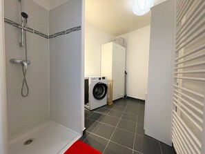 A bathroom with a shower, a washing machine, and a dryer.