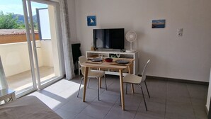 Et værelse med spisebord, stole, fjernsyn og ventilator.