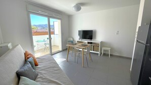 En moderne stue med sofa, spisebord, fjernsyn og en altan med bord og stole.
