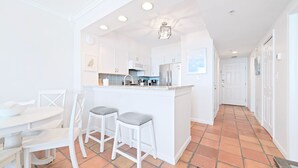 A bright kitchen with white cabinetry, a central island with stools, and a tiled floor. - Silver Beach 602 |  Updated, Direct Beach Front, Pet Friendly! (Orange Beach)