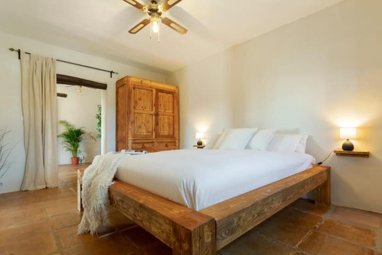 A bedroom with a wooden bed frame, a ceiling fan, a wooden wardrobe, and a bedside lamp.