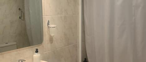 A bathroom with a sink, mirror, shower curtain, and a small shelf with toiletries.