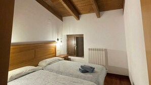 Une chambre avec un plafond en bois, un lit avec une tête de lit, une table de chevet, une fenêtre et un radiateur.