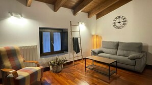 Un salon chaleureux avec un canapé à carreaux, un divan gris, une table basse en bois, une horloge murale et une fenêtre avec des rideaux.