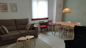 Una sala de estar con un sofá, dos mesitas, una mesa de comedor con sillas y una lámpara colgante.
