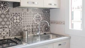 Una cocina pequeña con armarios blancos, un salpicadero estampado y un lavamanos de acero inoxidable.