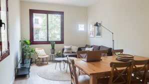 Un salón acogedor con sofá, mesa de comedor con sillas, una computadora portátil y un ventanal con vistas a la vegetación.