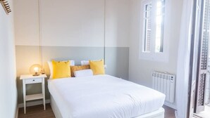 Un dormitorio con cama, mesita de noche y ventana.