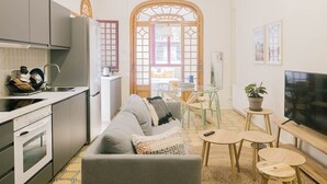 En kompakt opholdsstue med tekøkken, sofa, spiseplads og tv.