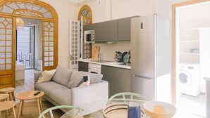 En kompakt bolig med tekøkken, sofa, spisebord og vaskemaskine.