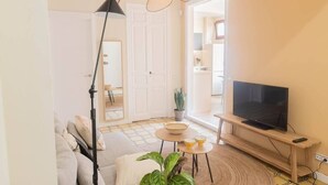 Un salon comprenant un canapé, une table basse, un téléviseur posé sur un meuble, une lampe sur pied et une porte donnant sur une autre pièce.