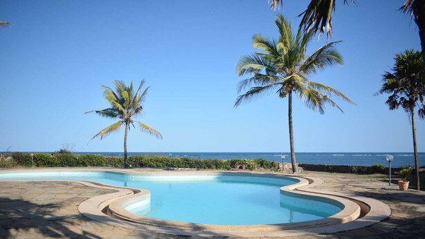 Une piscine à bordures courbes, entourée de carreaux de pierre, de palmiers et offrant une vue sur l’océan.