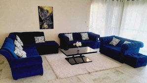 Un salon avec deux canapés bleus, une table basse et un tableau accroché au mur.