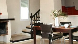 A dining area with a wooden table and chairs, a vase with flowers, and a kitchen in the background. - Denia: Appartement 1 Chambre avec Piscine, Clim et Parking à 500m de la Plage (Denia)