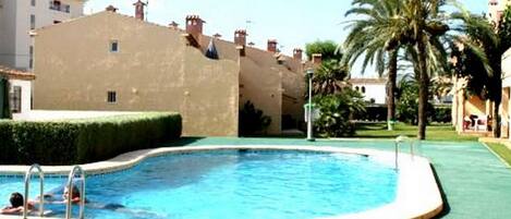 Una piscina de borde curvo, rodeada por un césped verde y palmeras.
