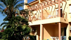 A two-story building with a balcony, surrounded by palm trees and a well-maintained lawn. - Denia: Appartement 1 Chambre avec Piscine, Clim et Parking à 500m de la Plage (Denia)