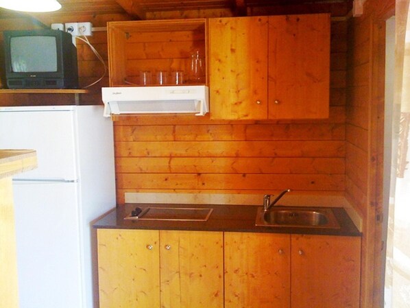 A compact kitchen with wooden cabinets, a built-in sink, and a small refrigerator.