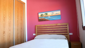 A bedroom with a wooden bed, a pink wall, and a painting of a beach scene. - Semi-detached house in Creixell with pool and WIFI, near beach (Creixell)
