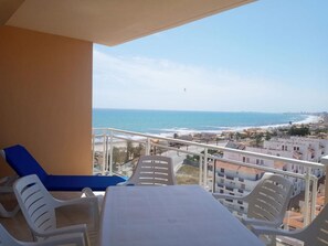 Relax on the balcony with a stunning ocean view, featuring a sandy beach and distant cityscape.