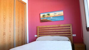 A bedroom with a wooden bed, a pink wall, and a painting of a beach scene. - Semi-detached houses in Creixell with pool, WiFi, parking, and air conditioning (Creixell)