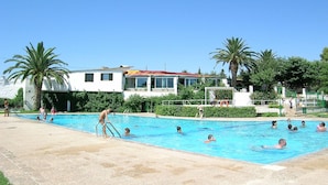 Zona de piscina con varias piscinas, palmeras y un edificio con techo rojo.
