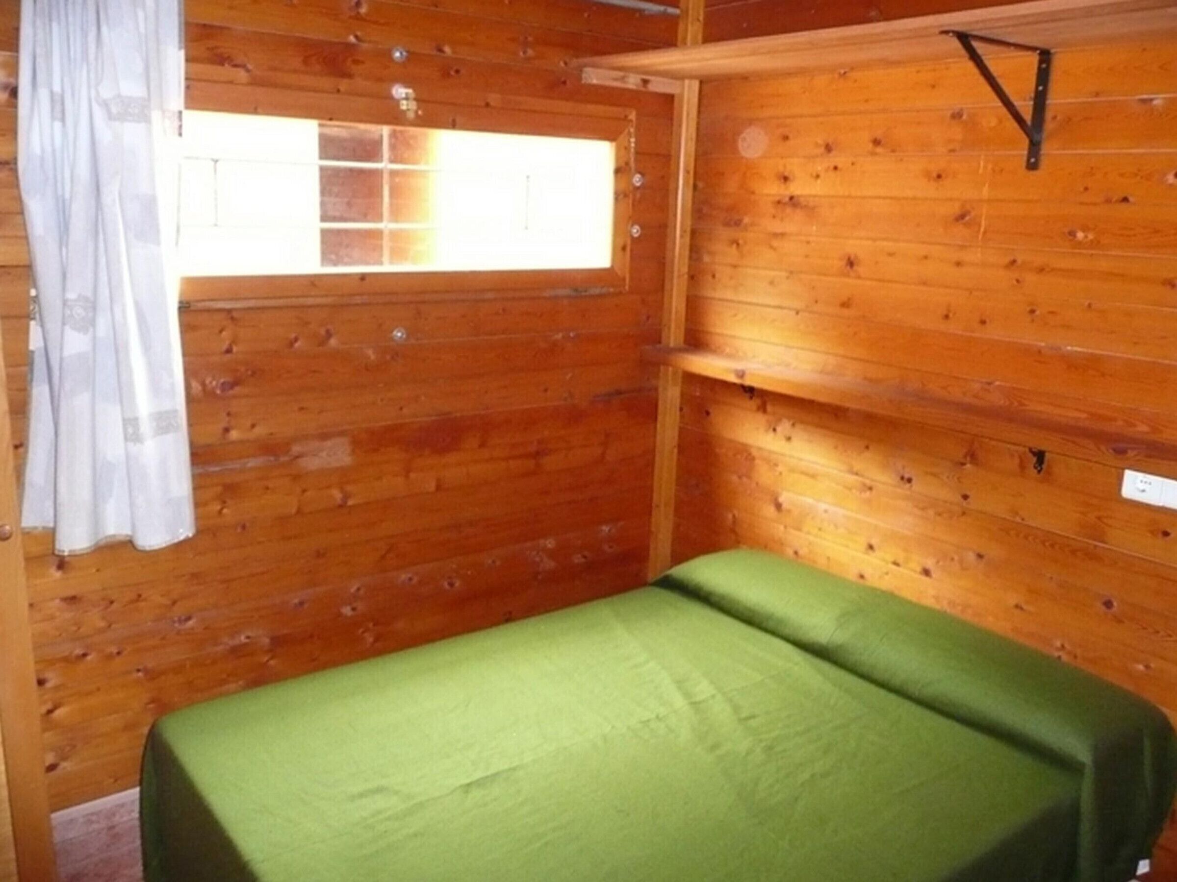 Una habitación de cabaña de madera con una cama, un ventanal y una cortina.