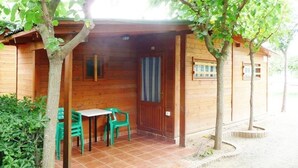 Een houten chalet met een betegeld terras, twee groene stoelen en een tafel.