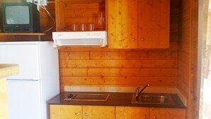 Een kleine keuken met houten kastjes, een inbouwspoelbak en een kleine koelkast.