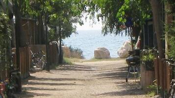 A dirt path leading to a beach with a wooden fence on one side and a barbecue grill on the other.